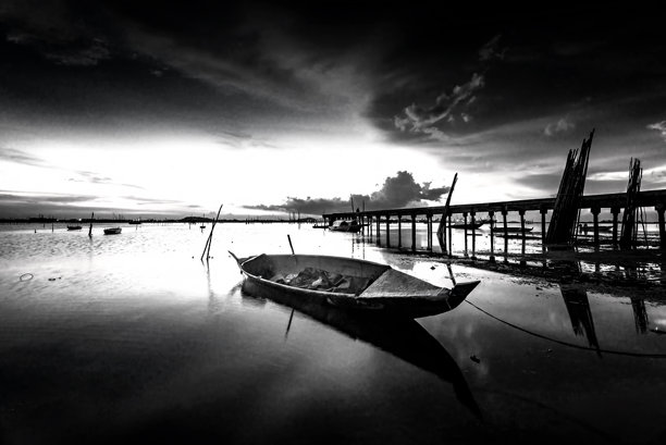 黑白照片，日落时分海上的桥。图片下载