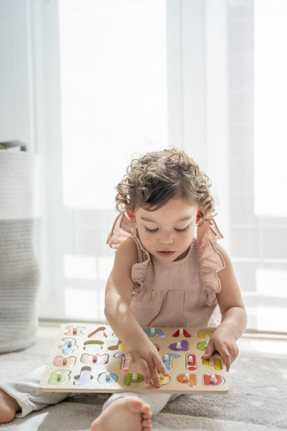 小女孩在房间里玩木制字母拼图的竖版照片。童年中的乐趣与学习。认知和运动技能的发展。蒙特梭利教育。图片下载