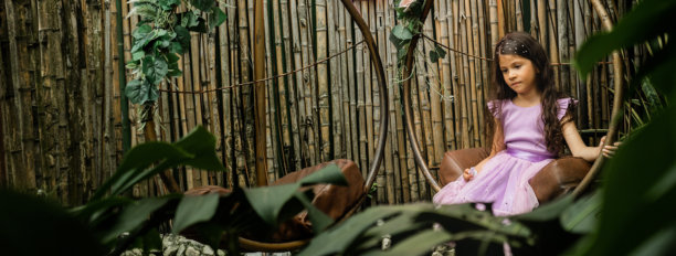 穿着淡紫色裙子的女孩在自然户外悬挂花园秋千上，周围是绿色的叶子 - 股票照片。图片下载