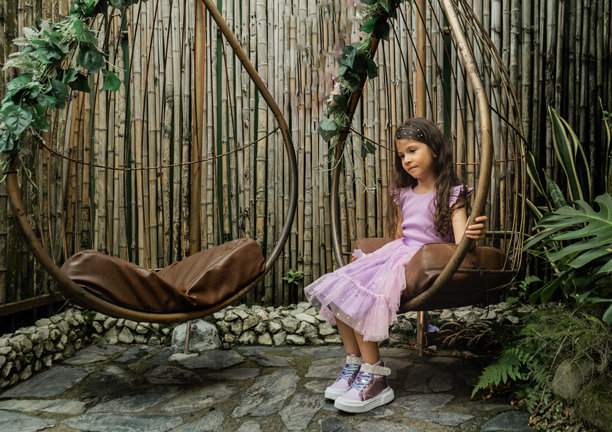 沉思的女孩坐在装饰秋千上，周围是竹子和自然植被，户外拍摄 - 股票照片。图片下载
