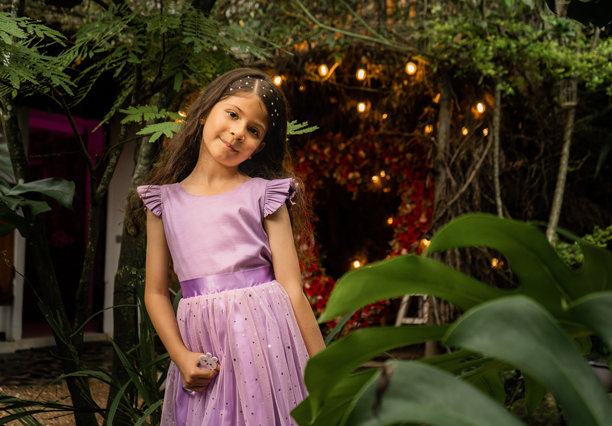 穿着淡紫色裙子的女孩在花园的一个神奇角落中，周围是灯光和花朵 - 股票照片。图片下载