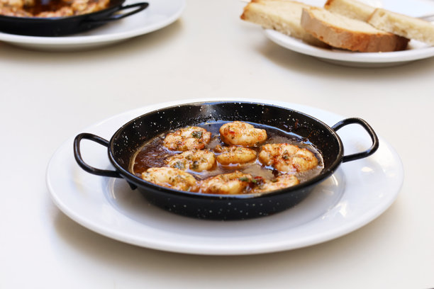 西班牙菜肴甘巴斯·皮尔皮尔，传统铸铁锅盛装，白色盘子放在桌面上的俯视照片图片下载