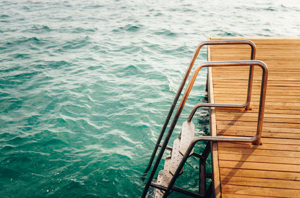 木质甲板和金属梯子通向碧蓝的海洋。夏季假期照片图片下载