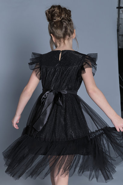 一个穿着黑色薄纱裙的小女孩优雅地旋转，展示了她服装背部的精美细节。这张图片捕捉了儿童正式时尚中运动的美感，突显了裙子的精致设计和流畅感。图片下载