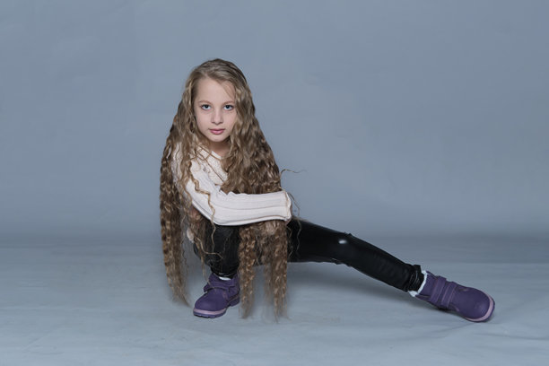 一个年轻女孩摆姿势，展现她的长发和丰富的质感，营造出一种俏皮和无忧无虑的氛围。这张图片宣传了儿童自然发型的美，鼓励温和护理、梳理和适当的发型维护习惯。图片下载