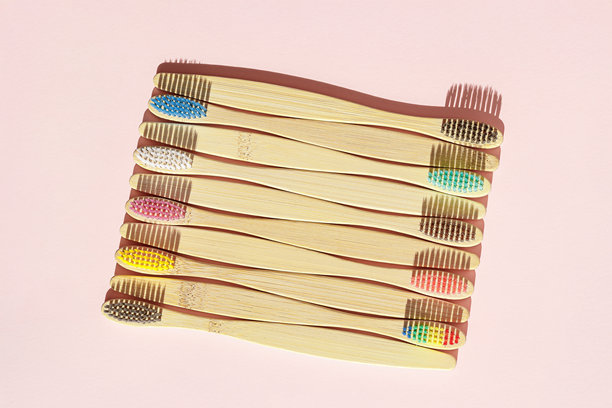 特写美学米色竹牙刷，彩色刷毛在粉色柔和背景下的阳光照射下。简约、卫生和环保替代品，俯视照片，极简风格。图片下载