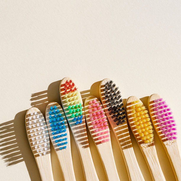 阳光下的米色背景上，环保木质牙刷配有柔软的彩色刷毛。极简设计照片，可持续卫生理念，零废弃生活方式，环保意识生活，强烈阴影。图片下载