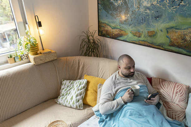 从上方拍摄的生病男子躺在床上使用手机的照片。留白空间。图片下载