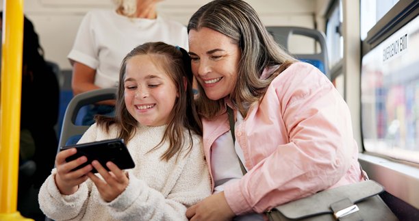 母亲和孩子在公交车上用手机观看视频、在线卡通和网络直播。快乐的家庭，女性和女孩在公共交通上旅行，通勤或冒险。图片下载