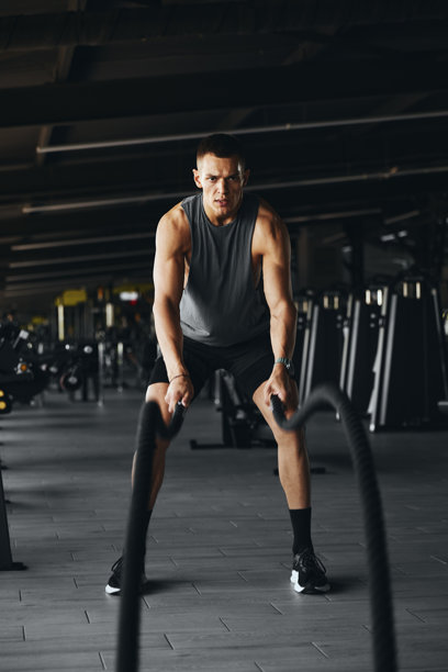 健身房内，一名运动员正在使用重型战绳进行全身训练的竖版照片图片下载