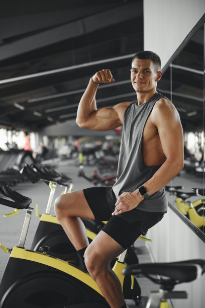 年轻男子穿着运动服，微笑着坐在自行车上，展示着二头肌的竖版照片图片下载