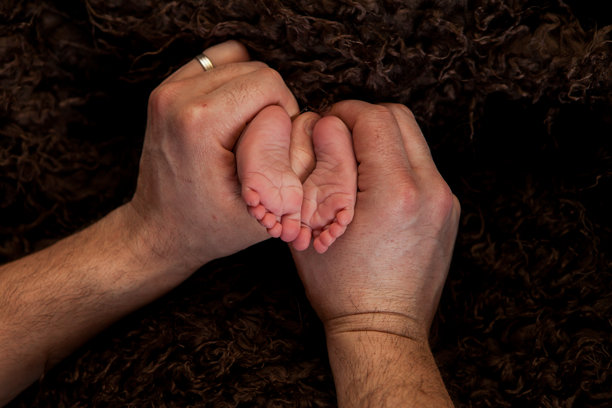 父母温柔的手中托着微小的新生儿脚，特写细节照片图片下载