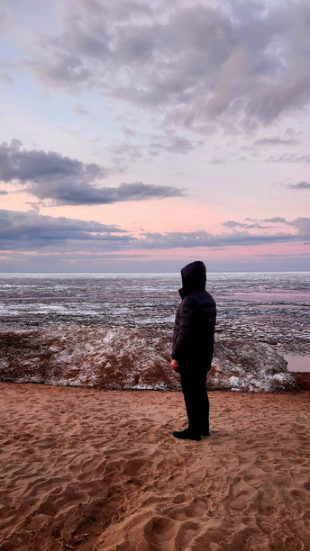 春季风景。美丽的黎明全景，海湾上方的积云在明亮的光线下。海岸线上有冰、雪和岩石。阳光的光芒在海面上反射。竖版照片图片下载