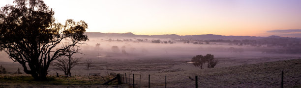 巨大的全景照片展示了第一缕曙光，乡村山谷被霜覆盖，柔和的雾气在清晨微光的色彩下缓缓流动。图片下载