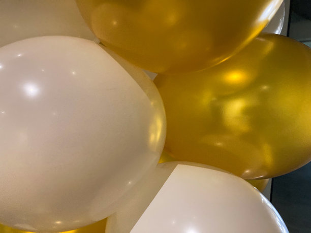 金色和白色的金属气球以不同的大小漂浮在室内墙壁的背景前，这是一张从低角度拍摄的简单照片。图片下载
