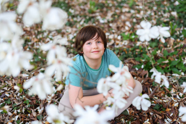穿着青绿色衬衫的可爱男孩在花瓣和春天的树叶中仰望。高质量照片图片下载