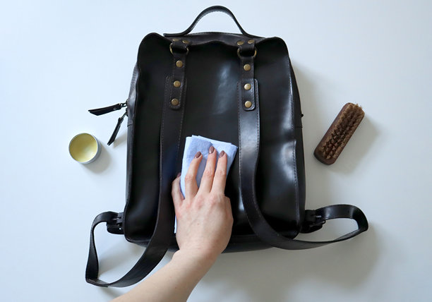 女人的手在清洁疯狂马皮背包。白色背景。照片。护理皮革制品。图片下载