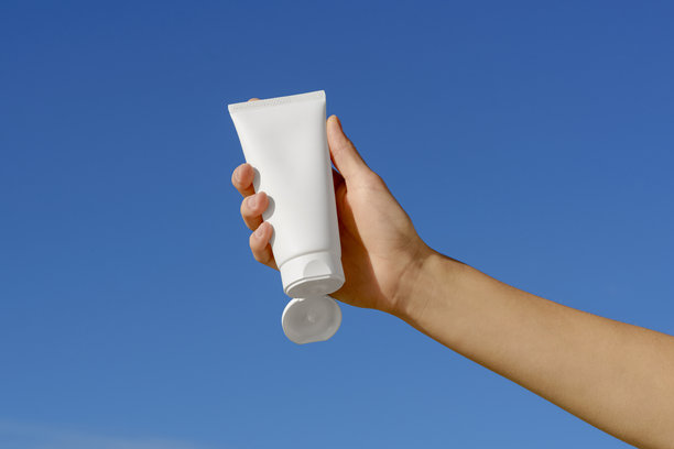 女性手握着白色的护肤霜空白管，背景为蓝天。美容、身体和面部护理的天然化妆品概念。适合您设计的图片。图片下载