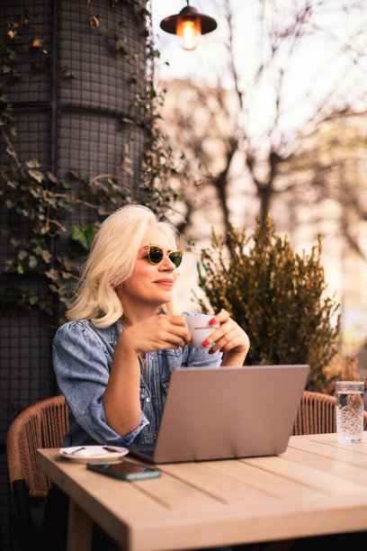 一位美丽的中年女性在咖啡馆花园里使用电脑并喝咖啡的照片。图片下载