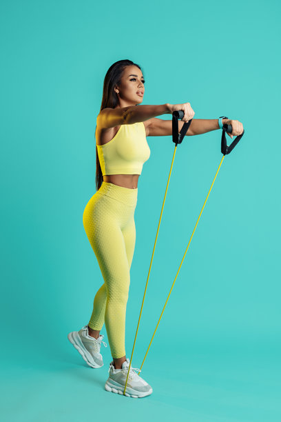 年轻女性在蓝色背景下用拉伸带训练肩部的全身照片。图片下载