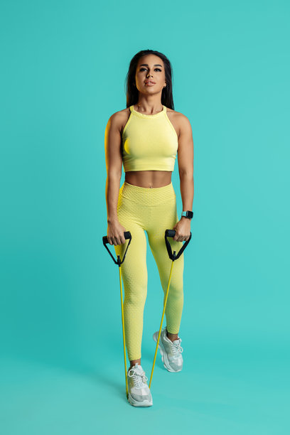 全身照片，运动年轻女性在蓝色背景下用拉伸带训练肩部。图片下载