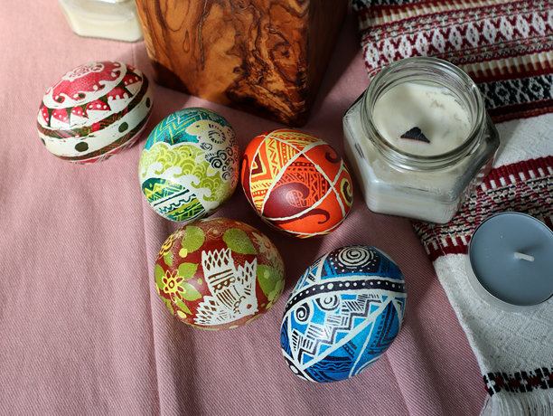 一组彩绘的复活节彩蛋。旁边有一支蜡烛。粉色背景和刺绣毛巾。照片。图片下载