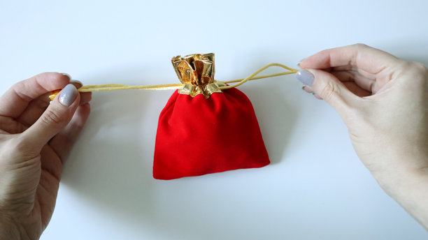 红色小袋子，配有金色抽绳。女性的手握紧袋子。白色背景。照片图片下载