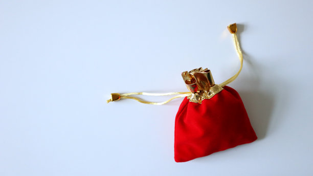 一个带金色抽绳的小红袋子。背景为白色，位于左上角。照片。图片下载