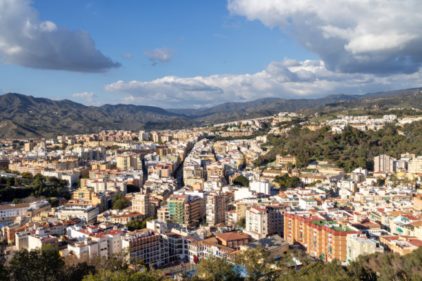 西班牙马拉加市街道的照片，展示了城市中心的鸟瞰图，背景是高层公寓楼和阳光明媚的山脉。图片下载