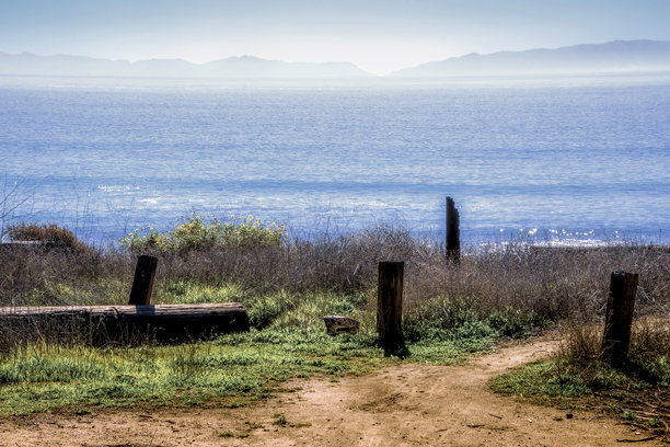 梦幻般的照片，前景是风景和古老的码头桩，背景是海洋和朦胧的岛屿。图片下载