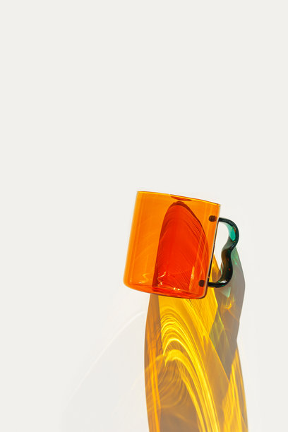 现代玻璃杯与明亮的阳光阴影，透明橙色饮品杯的极简照片。黄色反射，白色背景上的阴影，生活方式设计，家居装饰。图片下载