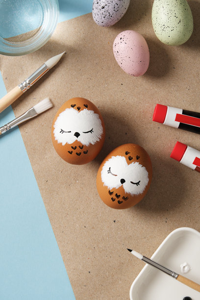 手绘的复活节彩蛋上有睡觉的猫头鹰，背景是颜料、画笔和调色板。DIY概念图片下载
