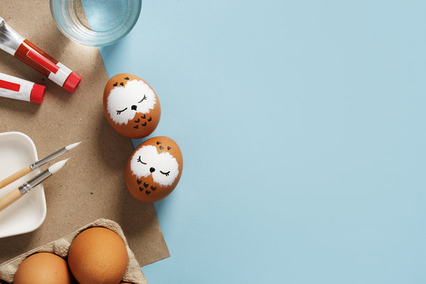 手绘的复活节彩蛋上有睡觉的猫头鹰，背景是颜料、画笔和调色板。留白空间。图片下载