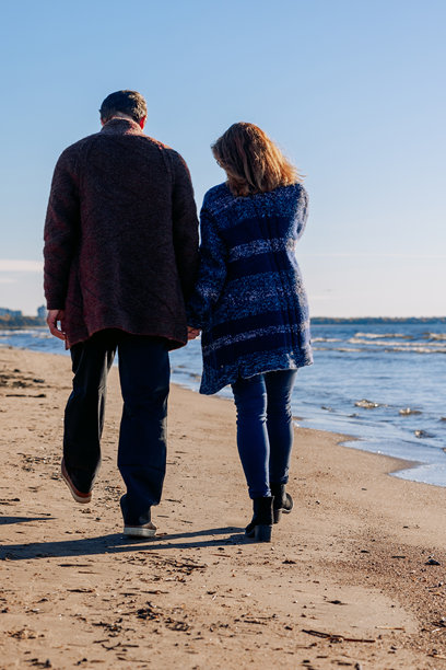 恩爱情侣在阳光明媚的秋日海滩上漫步。周末和生活方式的概念。竖版照片。背影。图片下载