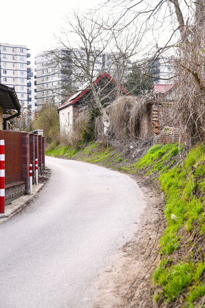照片展示了一条蜿蜒的沥青道路，穿过一座老建筑和一座现代高层建筑之间。图片下载
