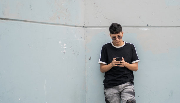 城市年轻人靠在墙上使用手机 - 股票照片。图片下载