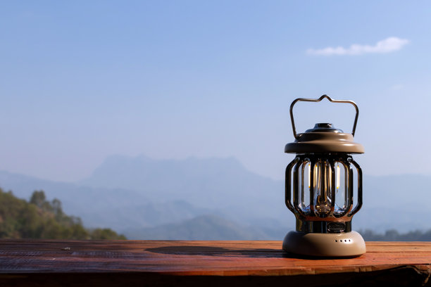 这张照片展示了一盏复古的灯笼放在木桌上，背景是一幅美丽的山景。图片下载