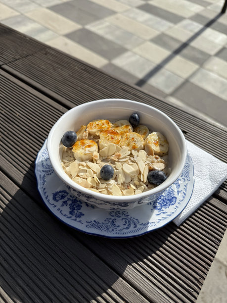 植物奶燕麦粥配焦糖香蕉、蓝莓和切片杏仁。素食餐概念。真实手机照片，强烈阳光，选择性对焦，非人工智能。图片下载