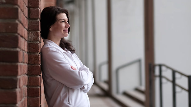 一位穿着白色夹克的女性自信地站在砖墙前，表情宁静。这张照片暗示了日常时刻中所找到的和谐，以及在忙碌环境中个人幸福的重要性。图片下载