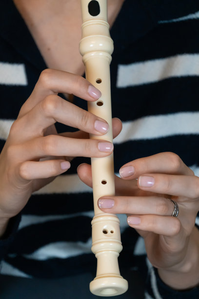 女性音乐家的手特写，轻柔地握着并演奏着直笛，展示了音乐才华、技巧和古典音乐的美。竖版照片图片下载