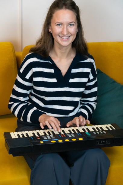 年轻女性音乐家坐在家中鲜艳的黄色沙发上，愉快地弹奏着小合成器，面带微笑，散发出对音乐的创造力和热情。竖版照片图片下载