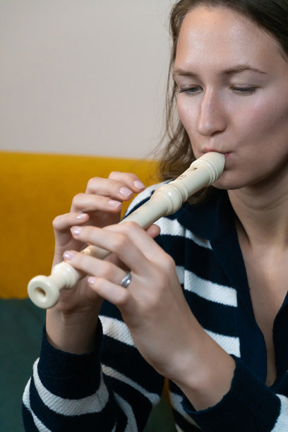 年轻女性音乐家坐在家中的黄色沙发上，吹奏着直笛，沉浸在创作美妙旋律的快乐中，享受着她最喜欢的爱好。竖版照片图片下载