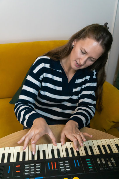 一位女性热情地演奏复古合成器，在温馨的家居环境中唤起音乐创意和怀旧感，背景有一张黄色沙发。竖版照片图片下载