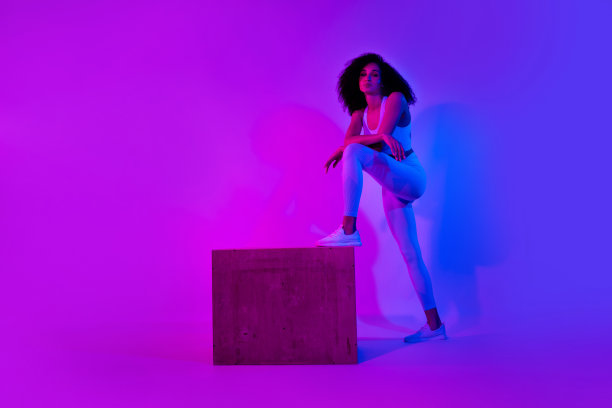 全身照片，运动生活教练女孩帮助你选择健身房的踏板，背景是五彩霓虹粉色视觉效果。图片下载