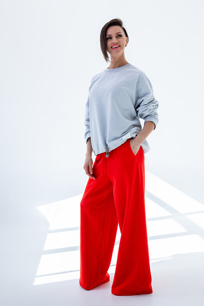 穿着灰色卫衣和红色裤子的年轻女性，背景为白色。工作室摄影。竖版照片。图片下载