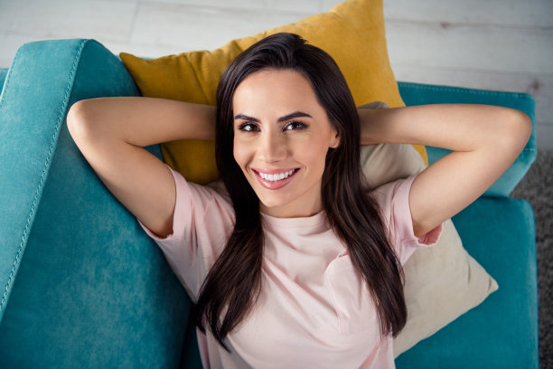 高角度拍摄的微笑漂亮女士躺在沙发上享受公寓假期的照片图片下载