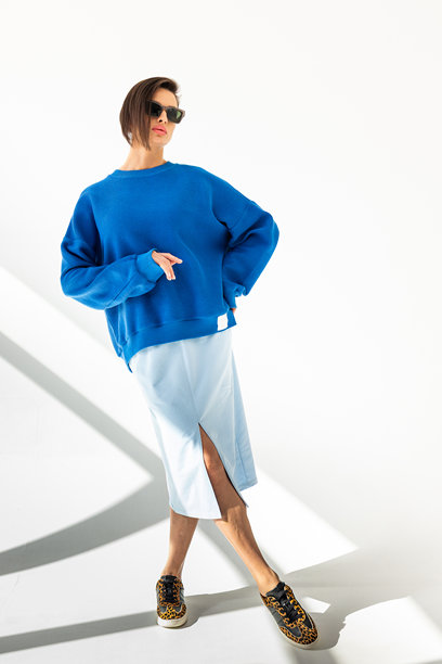 穿着蓝色卫衣和浅蓝色裙子的优雅女性，背景为白色。时尚女性风格。工作室摄影。竖版照片。图片下载