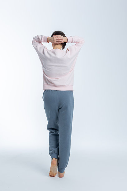 美丽的模特外貌女性。女孩穿着浅粉色毛衣和灰色裤子，背景为浅色。时尚妆容的漂亮女性在摄影棚中摆姿势。竖版照片。图片下载