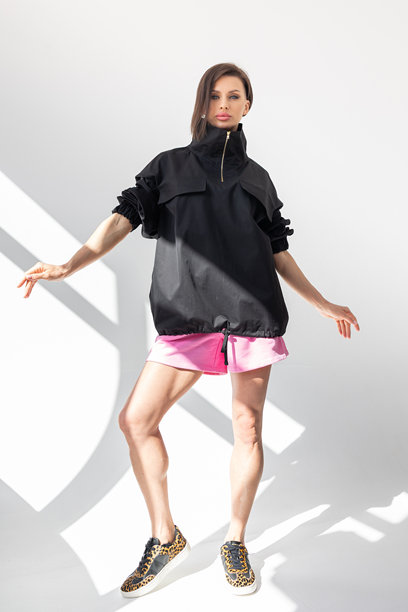 穿着黑色风衣和粉色短裤的优雅女性，背景为浅色。时尚女性风格。摄影棚拍摄。竖版照片。图片下载