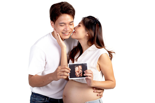 幸福的亚洲家庭夫妇在白色背景下，亚洲美丽的妻子亲吻她的丈夫，同时他们手中拿着超声波婴儿照片。美丽微笑的孕妇母亲，肚子隆起。图片下载